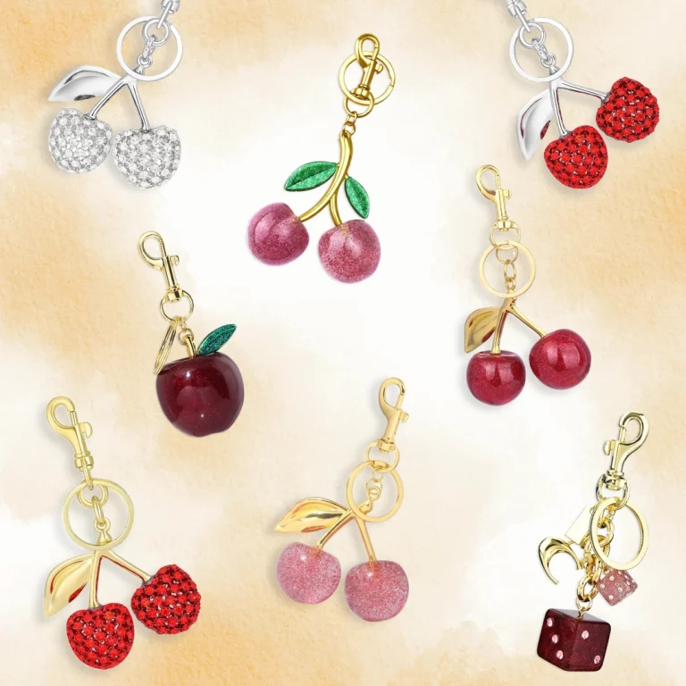 Cherry and fruit-themed keychains with rhinestones and glossy finishes in gold and silver tones on a neutral background